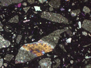 Un exemple de microscopie appliquée aux matériaux cimentaires : lame mince de béton. Les composants colorés sont des granulats ; le noir est la pâte de ciment. L’utilisation de la microscopie optique traditionnelle (lames minces pétrographiques) permet de contraster les différents composants et donc facilite leur identification.